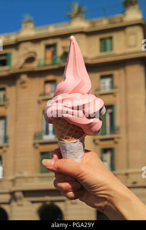 Colore rosa Lampone Soft servire il gelato cono essendo tenuto in mano, con sfocate edificio vintage a Santiago del Cile in background Foto Stock