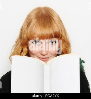 Un dai capelli rossi dagli occhi blu bambina guarda dalla lettura del suo libro. Foto Stock