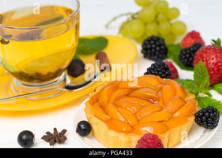 Pesche fresche crostata con il piccante tè al limone circondato da allentato di frutti di bosco freschi ed essiccati spezie Foto Stock