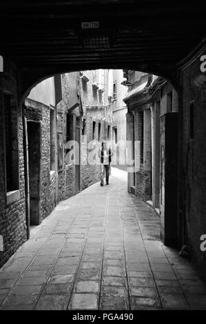 Venezia, Italia - 22 settembre 2016: uomo a camminare verso il basso una stretta viuzza centro di Venezia, Italia, monocromatico Foto Stock