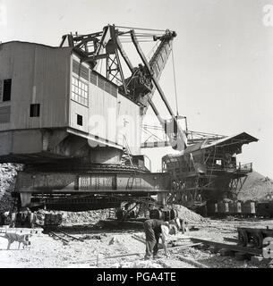 Degli anni Cinquanta, storico, un gigante escavatore industriale in una grande cava o buca, mineraria massa di argilla al Stewartby opere della London Brick Companyat Bedford, Inghilterra, Regno Unito. A questo tme i laterizi sono stati il più grande del mondo. La roccia sedimentaria formazione minati nel Bedfordshire, Oxford argilla, dominato il British industria del laterizio in questa epoca. Foto Stock