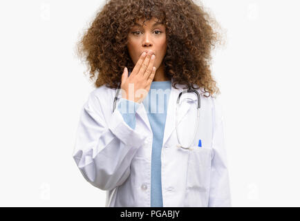 African American medico donna, medico professionale di lavoro copre la bocca in stato di shock, guarda timido, esprimendo il silenzio e confondere i concetti, paura Foto Stock