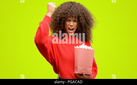 African American donna mangiare popcorn infastiditi e frustrato grida con rabbia, crazy e urla con la mano alzata, concetto di rabbia Foto Stock