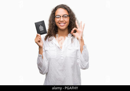 Giovane donna ispanica holding passaporto del Canada facendo segno ok con le dita, simbolo eccellente Foto Stock