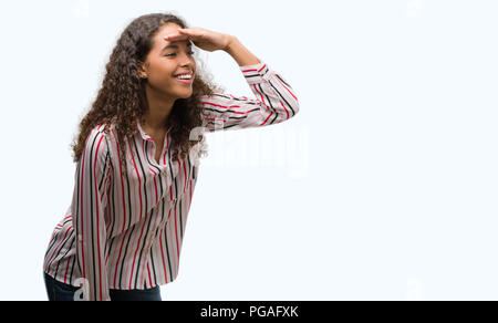 Giovane e bella donna ispanica molto felice e sorridente guardando lontano con la mano sopra la testa. Concetto di ricerca. Foto Stock