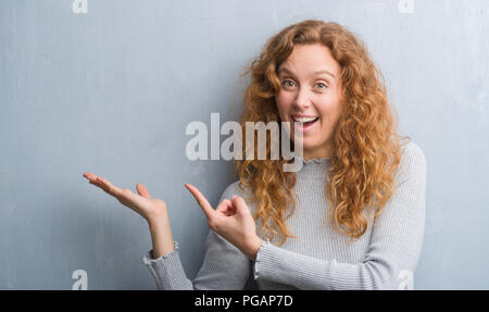 Giovane donna rosso su grigio parete grunge molto felice puntando con mani e dita Foto Stock