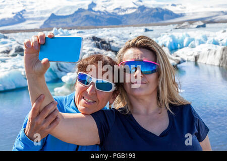 Due turisti femminile prendendo un selfie con uno smart phone in laguna Iceberg di Jokulsarlon Foto Stock