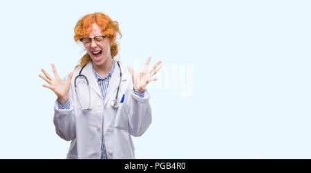 Giovani redhead donna che indossa uniformi medico celebrando mad e pazzo per il successo con le braccia sollevate e gli occhi chiusi urlando eccitati. Vincitore concept Foto Stock