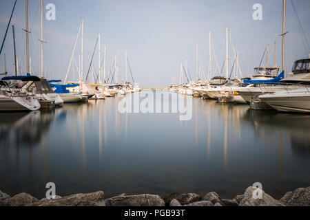 Lunga esposizione fotografia di barche a vela ancorata in un porto turistico di lisce come la seta acqua. Foto Stock