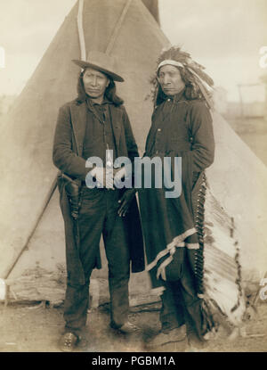 Due capi Oglala, American Cavallo (indossare abbigliamento occidentale e la pistola in fondina) e Red Cloud (INDOSSARE COPRICAPO) di intera lunghezza verticale, rivolto verso la parte anteriore, agitando le mani davanti tende Tepee--probabilmente su o in prossimità di Pine Ridge Prenotazione. Foto Stock