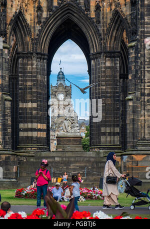 Edinburgh, Regno Unito - 27 Luglio 2018: persone passeggiando nei giardini di Princes Street e la vista del Balmoral attraverso il Monumento di Scott. Foto Stock