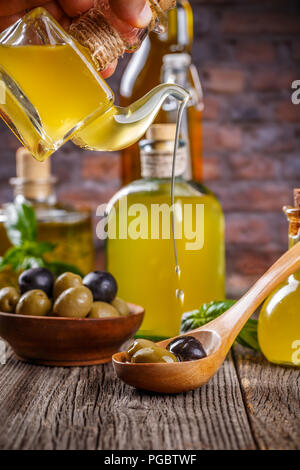 Olio extra vergine di oliva scorre su un cucchiaio di legno pieno di verde e di olive nere Foto Stock