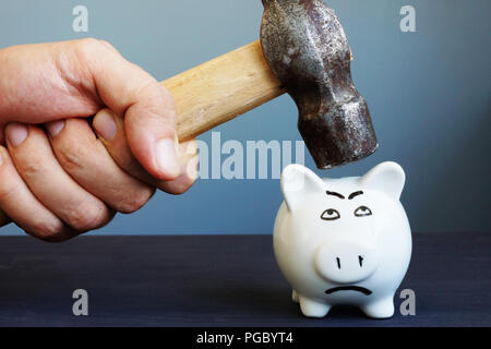Mano con un martello al di sopra di un salvadanaio. Problemi con il risparmio. Foto Stock
