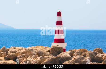 A strisce rosse e bianche mare faro di sicurezza fissati sulle rocce in porto con l'orizzonte di acqua in background in una limpida giornata di sole con un cielo blu Foto Stock