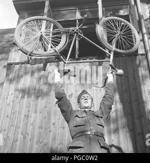 1940s soldato. Un giovane in uniforme sta equilibrando la bicicletta sopra la testa. Svezia 1943 Kristoffersson E90-1 Foto Stock