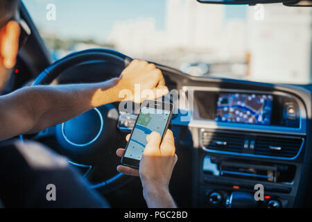 Chiusura del giovane uomo guardando il navigatore GPS dietro la ruota in auto. L uomo è messa a fuoco e il colore di primo piano e auto è su sfondo e sfocata. Vista posteriore Foto Stock