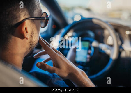 Chiusura del giovane uomo guardando il navigatore GPS dietro la ruota in auto. L uomo è messa a fuoco e il colore di primo piano e auto è su sfondo e sfocata. Vista posteriore Foto Stock