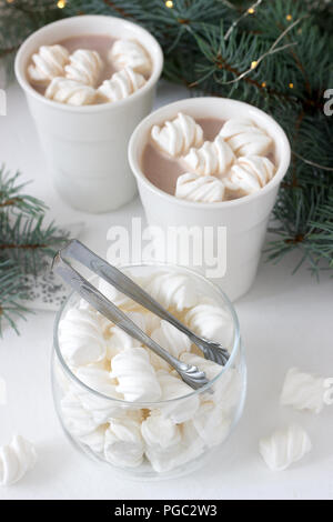 Il cacao con marshmelow in bianco tazze e marshmallows in un vasetto di vetro su un tavolo bianco con rami di abete rosso, una ghirlanda di fiori e una stella bianca. Messa a fuoco selettiva Foto Stock