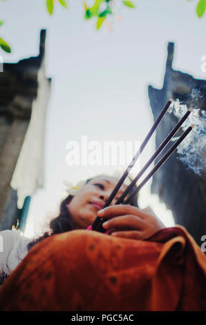 Bella donna asiatica holding bastoncini di incenso e pregando durante la cerimonia Indù in un tempio a Bali, in Indonesia Foto Stock