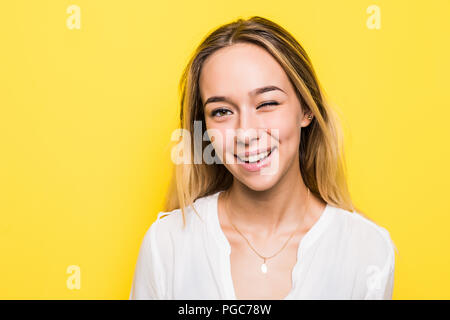 Cupo giovane donna bionda vestita casualmente a fare ritratti in telecamera, lampeggiante isolato su sfondo giallo Foto Stock