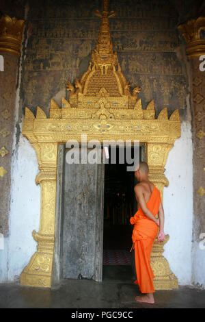 Monaco buddista di fronte a una porta in Wat Xieng Thong a Luang Prabang, Laos Foto Stock