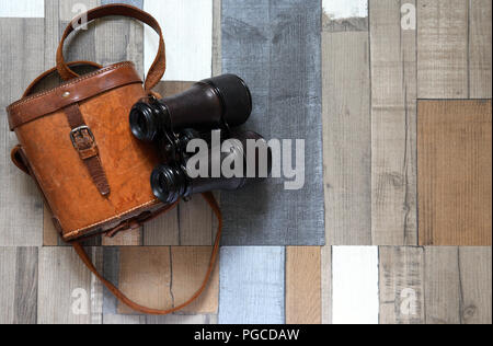 Vecchio binocolo con custodia di pelle sul colore di sfondo in legno Foto Stock