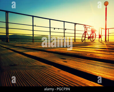 Silhouette di una bicicletta su un ponte sul mare al mattino. Golden tramonto sul mare costa. Sfondo dello stile di vita sulla spiaggia soleggiata, Nessebar, Bulgar Foto Stock