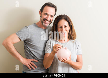 La mezza età matura, donna e uomo, tenendo salvadanaio con una faccia felice in piedi e sorridente con un sorriso sicuro che mostra i denti Foto Stock