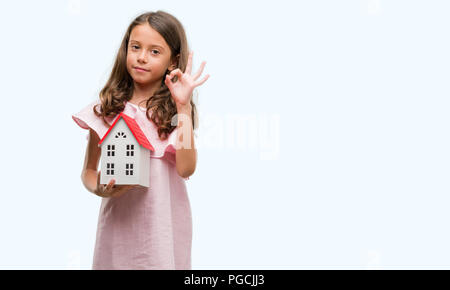 Bruna ragazza ispanica azienda piccola casa facendo segno ok con le dita, simbolo eccellente Foto Stock