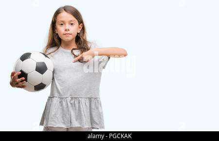 Bruna ragazza ispanica holding soccer football palla con sorpresa faccia puntare il dito a se stesso Foto Stock