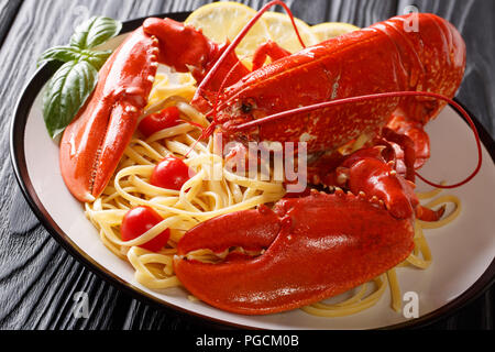 Costoso e spaghetti aragosta cotte, pomodoro, limone e erbe aromatiche fresche di close-up vengono serviti su una piastra orizzontale. Foto Stock