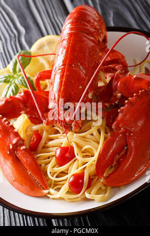 Servite gli spaghetti con red lobster, pomodoro, limone e erbe aromatiche fresche di close-up su una piastra su uno sfondo nero. In verticale Foto Stock