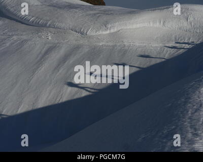 Vista laterale di due sciatori con zaini passeggiate sulla neve in presenza di luce solare. Ombra di quattro persone colata su neve. Foto Stock