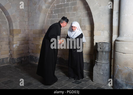 Sacerdote e nun raccontando gossip negli angoli di una chiesa medievale Foto Stock