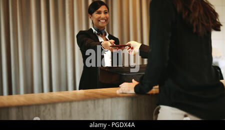 Donna sorridente concierge il ritorno dei documenti all'hotel valutazione dopo il processo di check-in. Client femmina riceve i suoi documenti alla reception Foto Stock