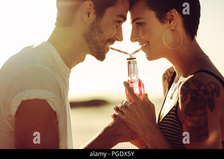 Close up di coppia giovane in amore di bere drink freddo dalla stessa bottiglia. L uomo e la donna sorpresa in un bel momento, la condivisione di una bevanda. Foto Stock