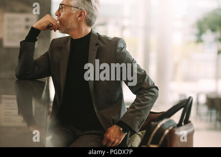 Ritratto di imprenditore senior seduto presso il cafe. Senior uomo nel business suit che guarda lontano mentre è seduto presso la caffetteria. Foto Stock