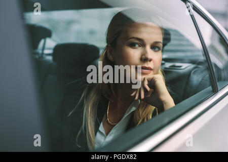 Fiducioso giovane imprenditrice seduta sul sedile posteriore di un taxi e guardando fuori dalla finestra. Executive femmina che viaggiano da un'auto. Foto Stock