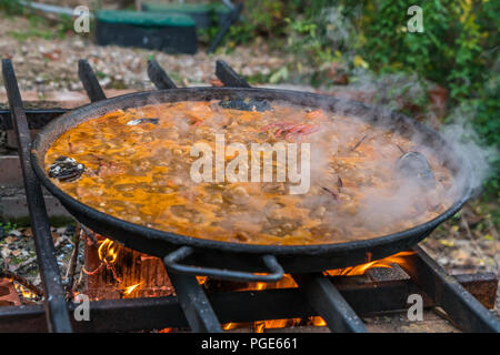 Tipica paella spagnola cotto naturale sul fuoco di legna e carbone in un tradizionale camino. Seafod, calamari, cozze, gamberi, granchi e i fagiolini verdi Foto Stock