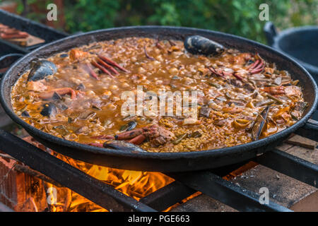 Tipica paella spagnola cotto naturale sul fuoco di legna e carbone in un tradizionale camino. Seafod, calamari, cozze, gamberi, granchi e i fagiolini verdi Foto Stock
