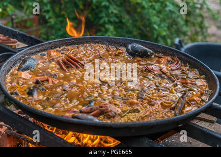 Tipica paella spagnola cotto naturale sul fuoco di legna e carbone in un tradizionale camino. Seafod, calamari, cozze, gamberi, granchi e i fagiolini verdi Foto Stock
