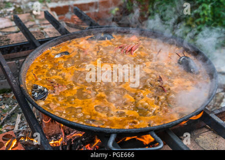 Tipica paella spagnola cotto naturale sul fuoco di legna e carbone in un tradizionale camino. Seafod, calamari, cozze, gamberi, granchi e i fagiolini verdi Foto Stock