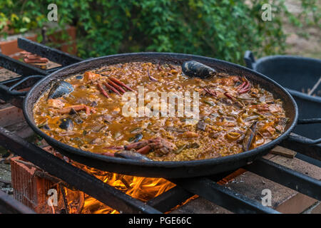 Tipica paella spagnola cotto naturale sul fuoco di legna e carbone in un tradizionale camino. Seafod, calamari, cozze, gamberi, granchi e i fagiolini verdi Foto Stock