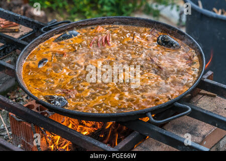 Tipica paella spagnola cotto naturale sul fuoco di legna e carbone in un tradizionale camino. Seafod, calamari, cozze, gamberi, granchi e i fagiolini verdi Foto Stock