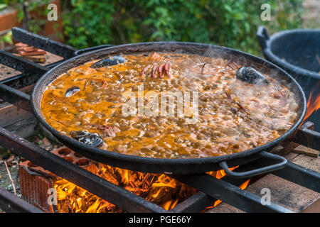 Tipica paella spagnola cotto naturale sul fuoco di legna e carbone in un tradizionale camino. Seafod, calamari, cozze, gamberi, granchi e i fagiolini verdi Foto Stock