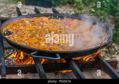 Tipica paella spagnola cotto naturale sul fuoco di legna e carbone in un tradizionale camino. Seafod, calamari, cozze, gamberi, granchi e i fagiolini verdi Foto Stock