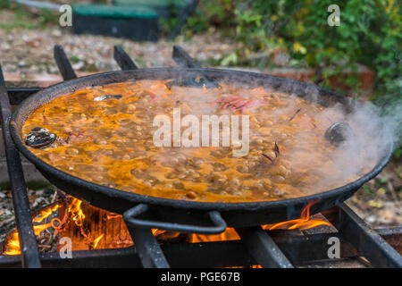 Tipica paella spagnola cotto naturale sul fuoco di legna e carbone in un tradizionale camino. Seafod, calamari, cozze, gamberi, granchi e i fagiolini verdi Foto Stock