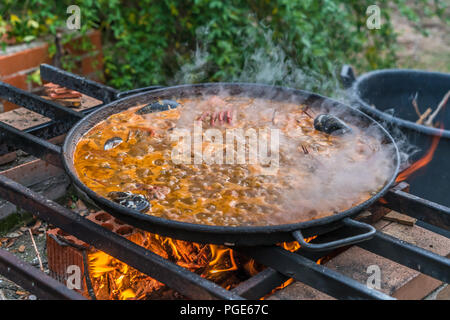 Tipica paella spagnola cotto naturale sul fuoco di legna e carbone in un tradizionale camino. Seafod, calamari, cozze, gamberi, granchi e i fagiolini verdi Foto Stock
