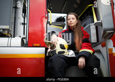 Foto del giovane fire donna con capelli lunghi in tuta siede in camion dei pompieri Foto Stock