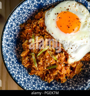 Kimchi fried rice (bokkeumbap) con un uovo fritto in azzurro e bianco ciotola, shot flat-lay Foto Stock